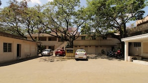 A courtyard with a paved ground, parked cars, and a building with multiple floors and windows. - Sibi Lodge (Coimbatore)