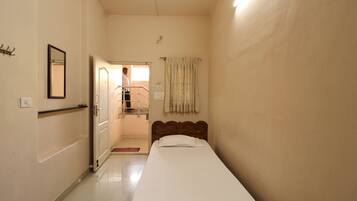 Habitación de hotel estrecha con una cama individual, un baño pequeño y una puerta que da a un balcón.