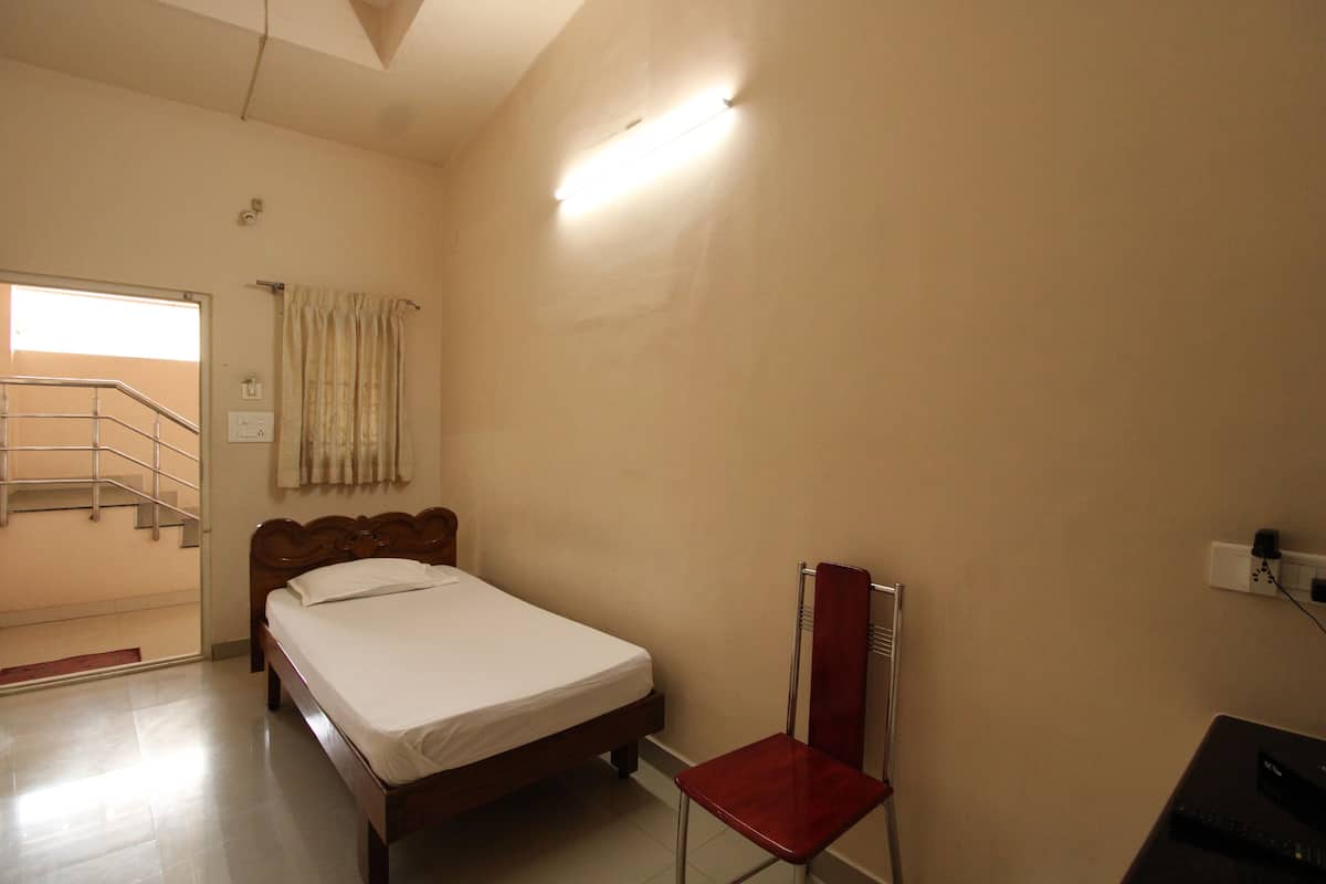 Quarto com cama, poltrona, radiador, tomada e porta que dá para uma escadaria.