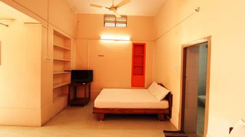 A compact room with a bed, a television on a small table, and a ceiling fan.