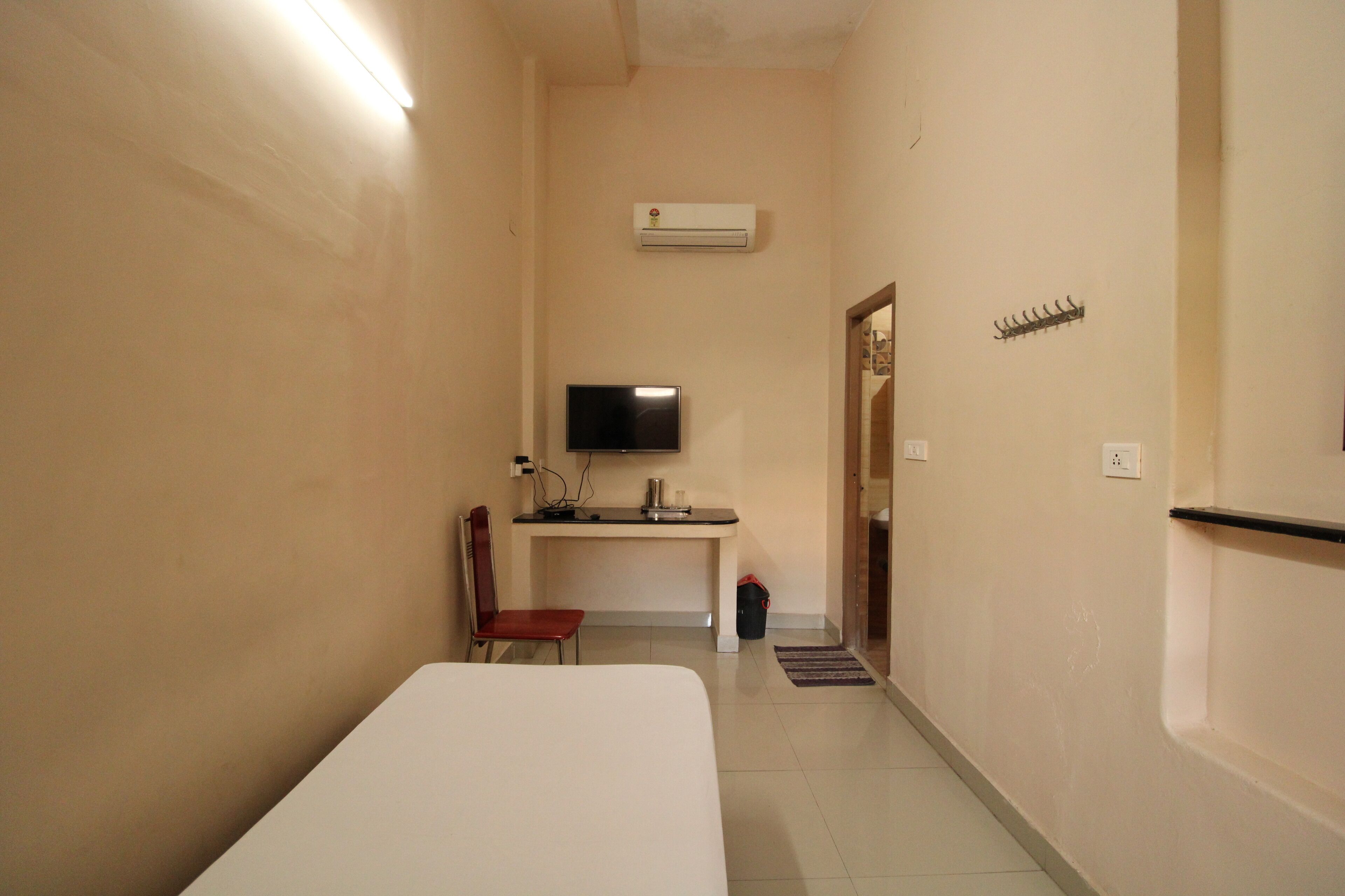 A narrow hallway with a bed, a desk, a chair, and a television.