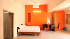 A bedroom with a bed, desk, chair, and a ceiling fan. - Sibi Lodge (Coimbatore)