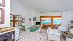 Ein modernes Wohnzimmer mit Essbereich, weißen Möbeln, einem Fernseher und gerahmten Kunstwerken an den Wänden.