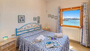 Ein Schlafzimmer mit Bett, Nachttisch, Fenster mit Meerblick und gerahmten Bildern an der Wand.