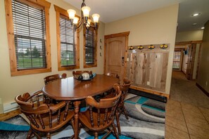 A dining room with a wooden table and chairs, a chandelier, and a door with a coat rack.