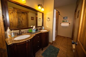 A bathroom with two sinks, a large mirror, wooden cabinets, and a shower area.