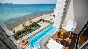 Un balcón con piscina, una silla blanca y una mesa con bebidas.