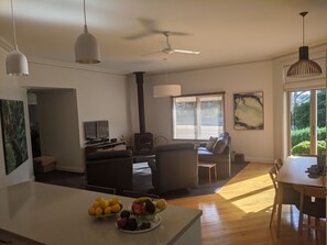 A spacious living area with a fireplace, a dining table, and a kitchen island with fruit. - Foxhouse (Aireys Inlet)