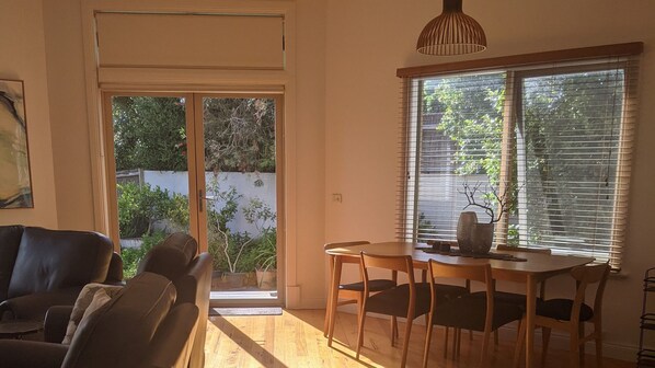 A room with a sliding glass door leading to a garden, a dining table with chairs, and a hanging light fixture.