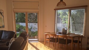 Ein Zimmer mit Esstisch, Stühlen, einer Couch und einem großen Fenster mit Jalousien.