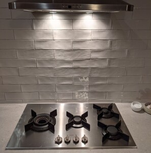 A stainless steel gas stove with four burners and a hood above it. - Foxhouse (Aireys Inlet)