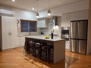 A modern kitchen with a central island, stainless steel appliances, and wooden flooring. - Foxhouse (Aireys Inlet)