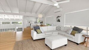 A spacious living area with a white sectional sofa, a wooden coffee table, and a large window with a view of the outdoors. - Peppertree Jervis Bay - Pet Friendly Beachfront with Sea Views (Callala Beach)