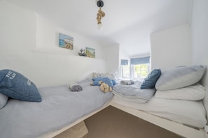 Quarto com duas camas, janela com cortinas e prateleira na parede com quadros.