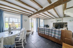 Um quarto com lareira de pedra, um sofá, uma mesa de jantar com cadeiras e um cão.
