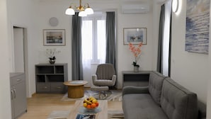 Una sala moderna con un sofá gris, una mesa de centro de madera con fruta, un sillón gris y una mesita redonda.