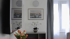 Una sala de estar moderna con un televisor de pantalla plana, una mesa de centro redonda de madera, un jarrón con flores y un gran ventanal con cortinas.