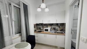 Una cocina compacta con armarios blancos, microondas, lavamanos y comedor con mesa y sillas.
