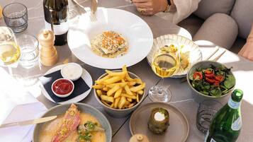 Een eettafel met verschillende gerechten, waaronder vis, friet en een salade, plus wijnglazen en flessen.
