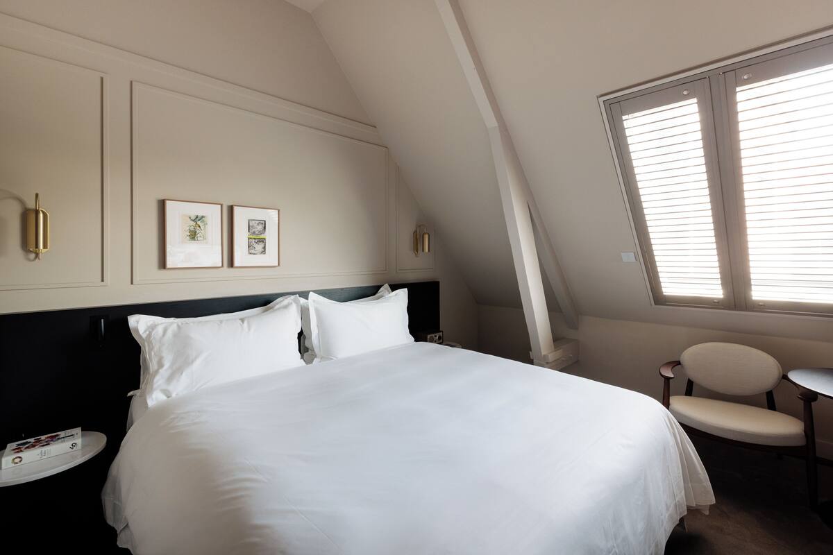 A hotel room with a large bed, a small round table, and two framed pictures on the wall.