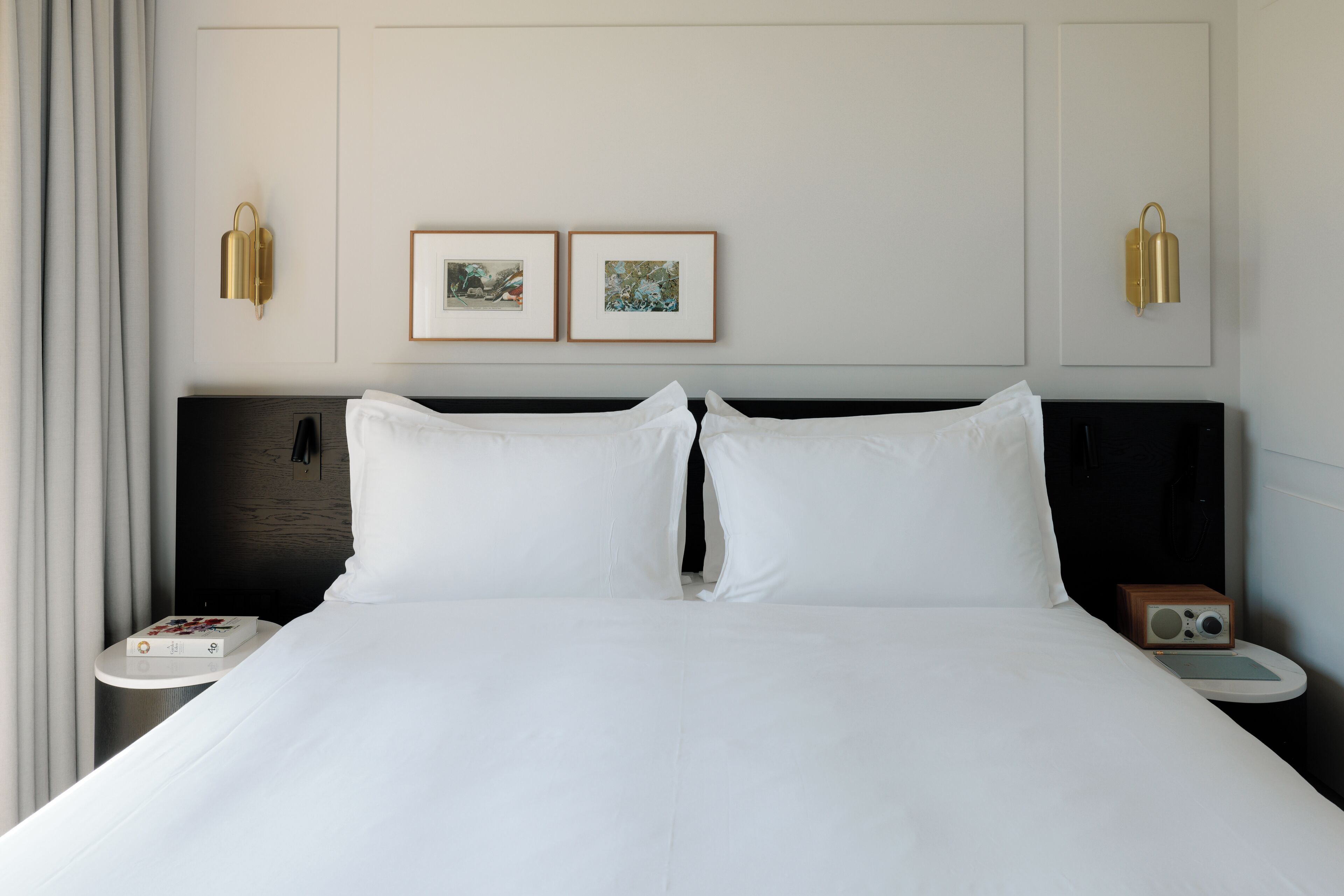 A hotel room with a large bed, two framed pictures on the wall, and a bedside table with a radio.