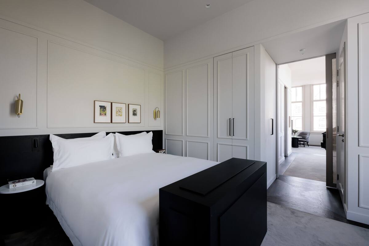 A hotel room with a large bed, a bedside table, a black TV stand, and a wardrobe.