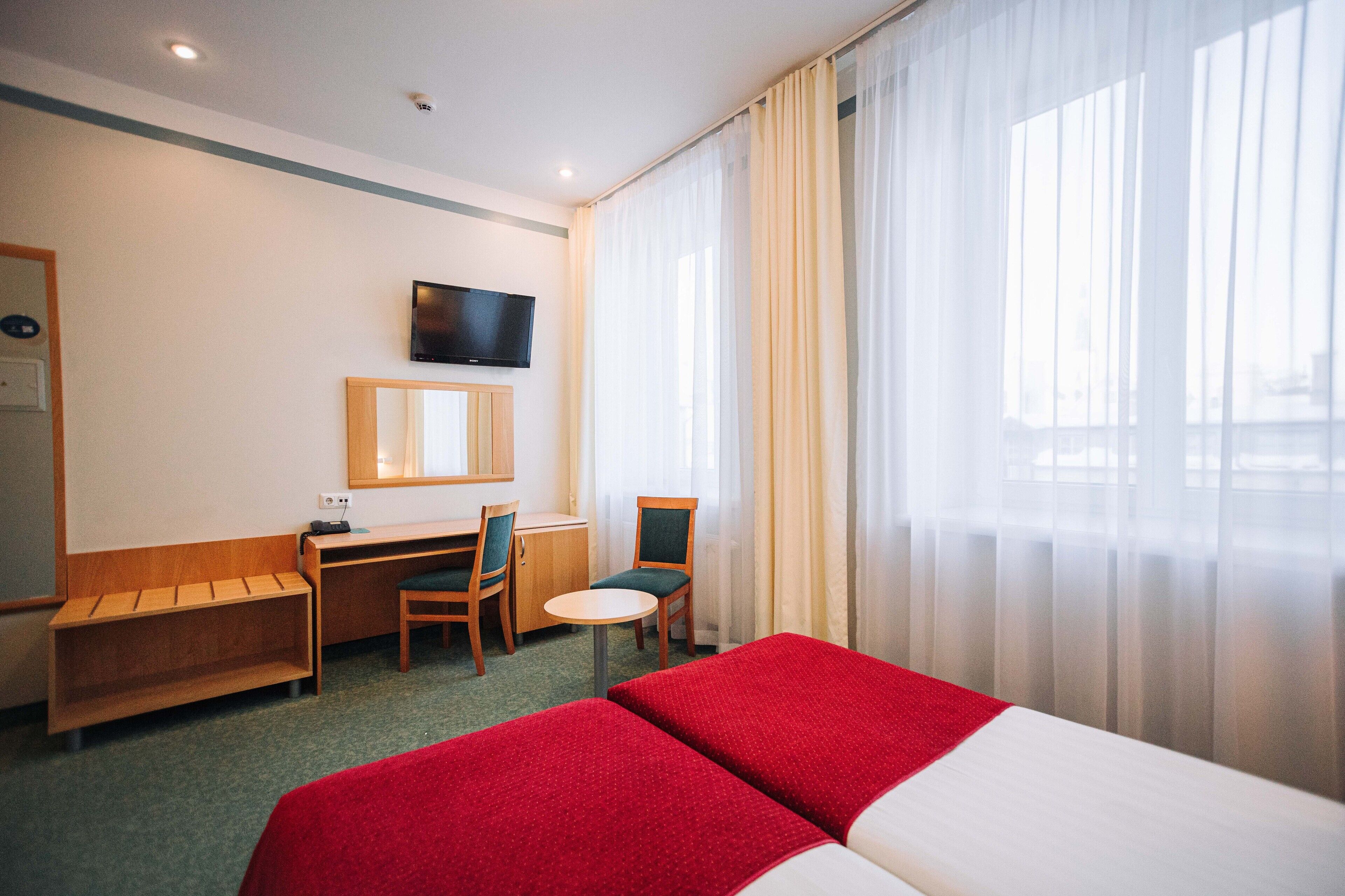 Una camera d'albergo con un letto, una scrivania, una sedia, un televisore e una finestra con tende.