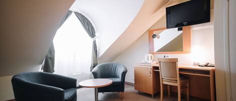 Una habitación de hotel con escritorio, dos sillas, televisor y ventana con cortinas.