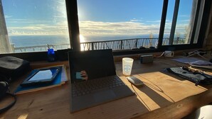 A laptop on a wooden desk with a view of the ocean through large windows. - Unique sunrise oceans' view (Nordeste)