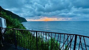 A coastal view with a balcony overlooking the sea, a house on the left, and a mountainous backdrop. - Unique sunrise oceans' view (Nordeste)