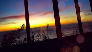 A sunset view through window frames, with silhouettes of vegetation and a calm sea. - Unique sunrise oceans' view (Nordeste)