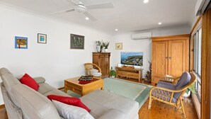 A living room with a sofa, a wooden cabinet, a television, and a view of a coastal town.