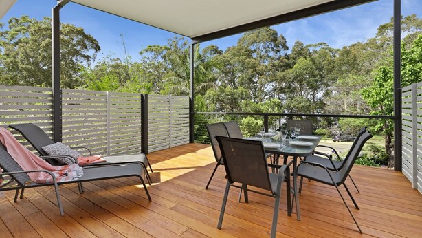 An outdoor patio with a wooden deck, metal chairs, a table set for dining, and a view of trees and greenery.