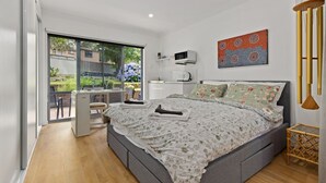 A bedroom with a large bed, a desk, and a view of the garden.