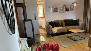 A living room with a sofa, coffee table, and a vase of tulips. There are framed pictures on the wall and a window with a view. - Vacation bungalow in Steinbach-Hallenberg (Steinbach-Hallenberg)