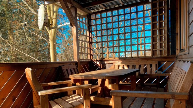 A wooden deck with a table and chairs, a wooden fence, and a view of trees through a lattice window. - Vacation bungalow in Steinbach-Hallenberg (Steinbach-Hallenberg)
