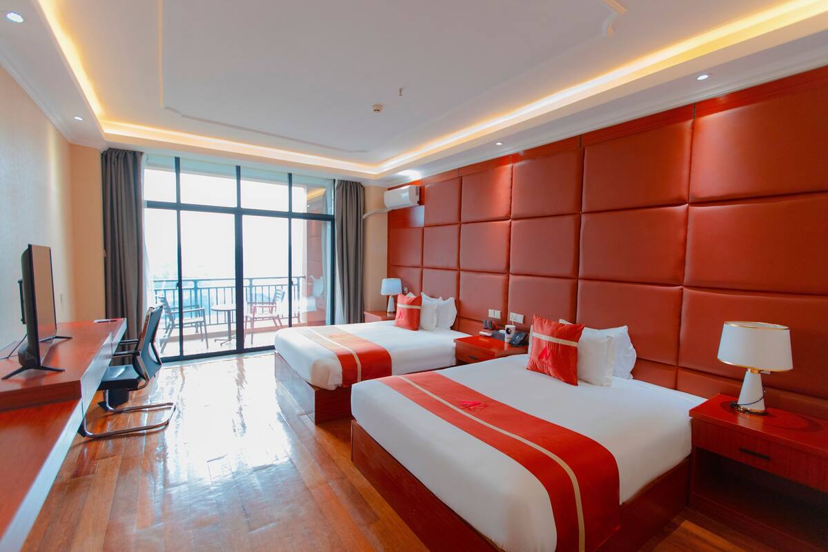 A hotel room with two beds, a TV, a desk, and a balcony view.