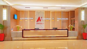 Een hotel receptie met een marmeren balie, een aan de muur bevestigde televisie en potplanten.