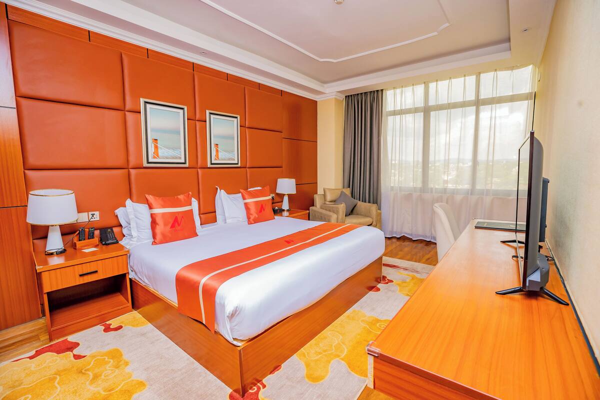 A hotel room with a large bed, a desk, a chair, and a TV.