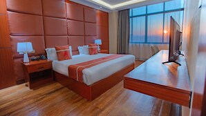 Een hotelkamer met een groot bed, een houten hoofdeinde, nachtkastjes met lampen, een bureau en een televisie.