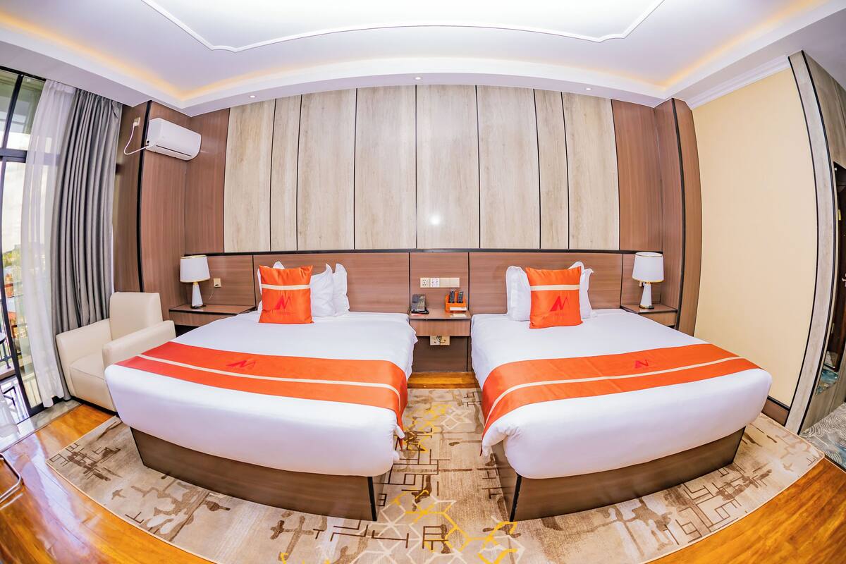 A hotel room with two beds, a sofa, a desk, and a large window.
