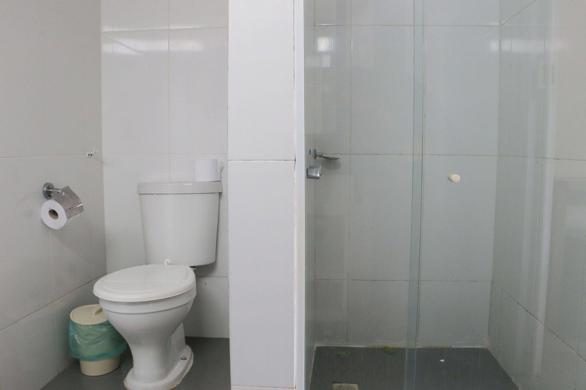A bathroom with a toilet, a glass shower enclosure, and a trash bin.