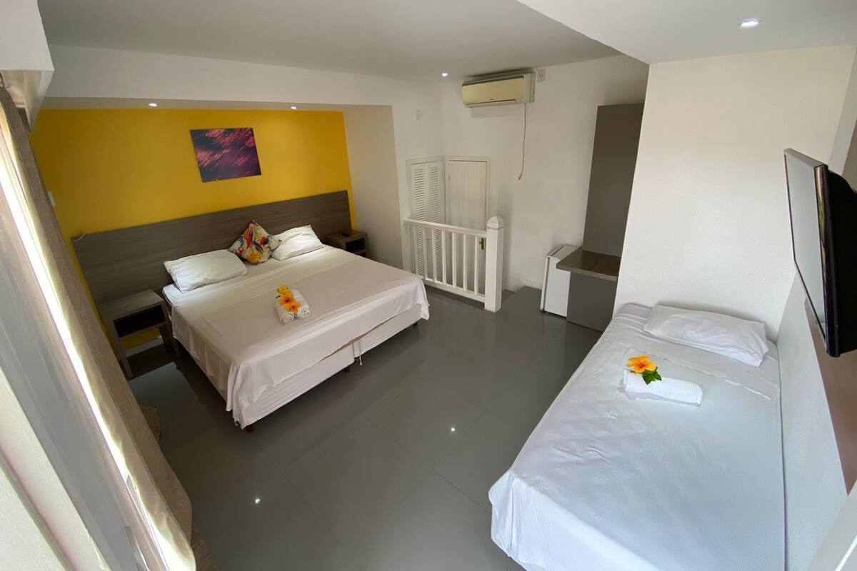 A hotel room with two beds, a white ceiling, a yellow accent wall, and an air conditioning unit.