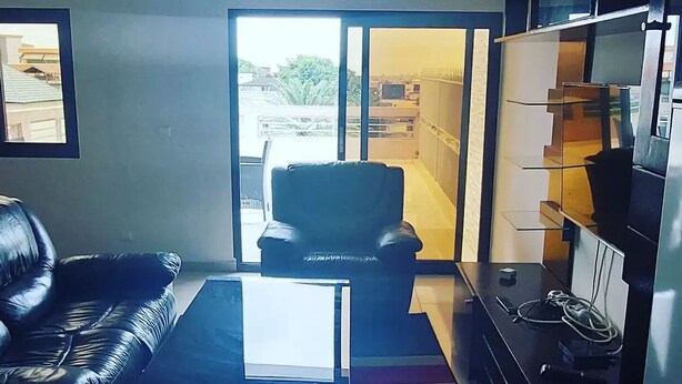Een woonkamer met een leren bank, een salontafel, een tv-meubel en een schuifpui naar een balkon.