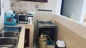Een kleine keuken met een gasfornuis, een spoelbak, een magnetron en een kast boven het aanrecht.