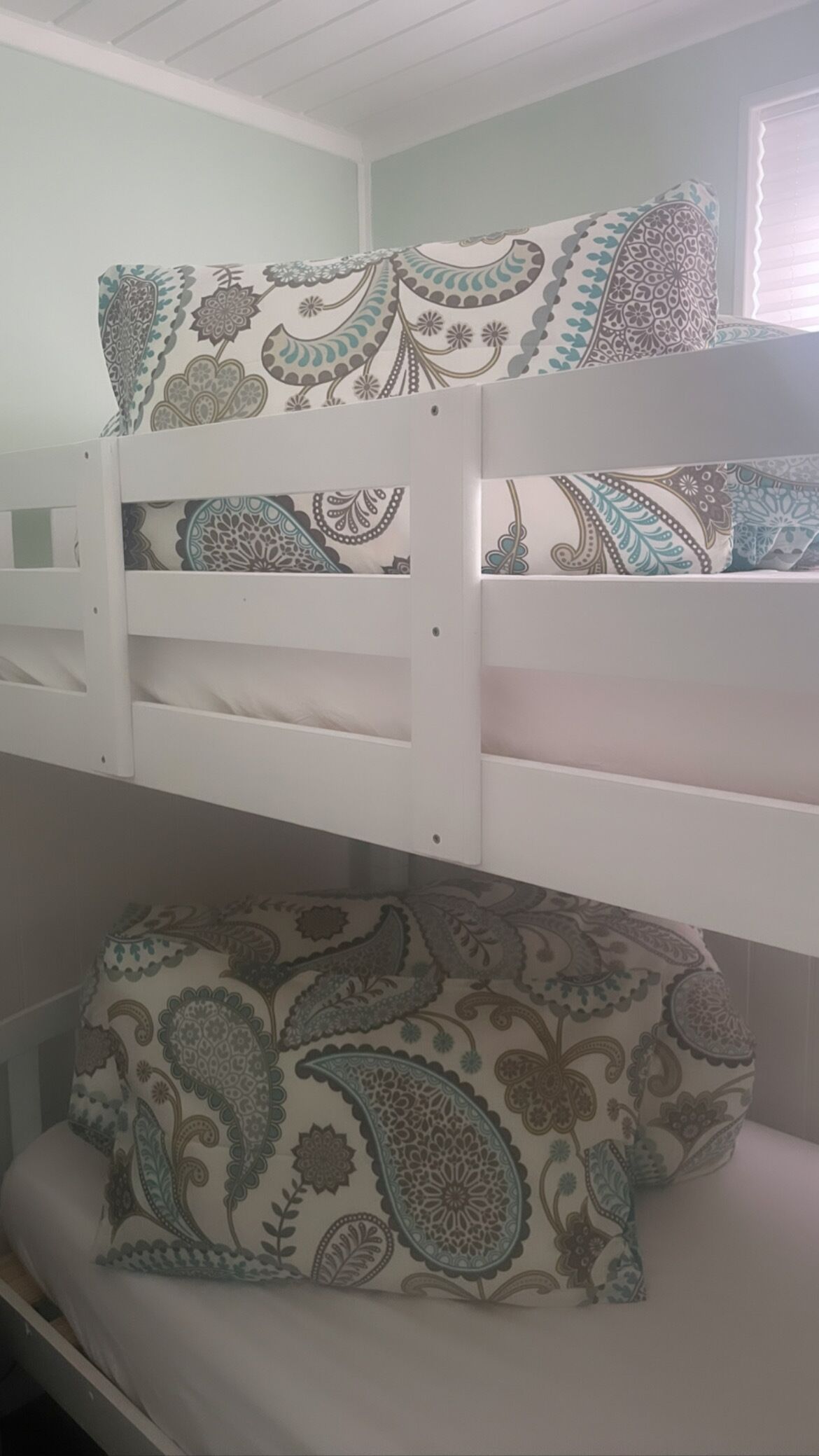A bunk bed with patterned bedding in a room with a window.