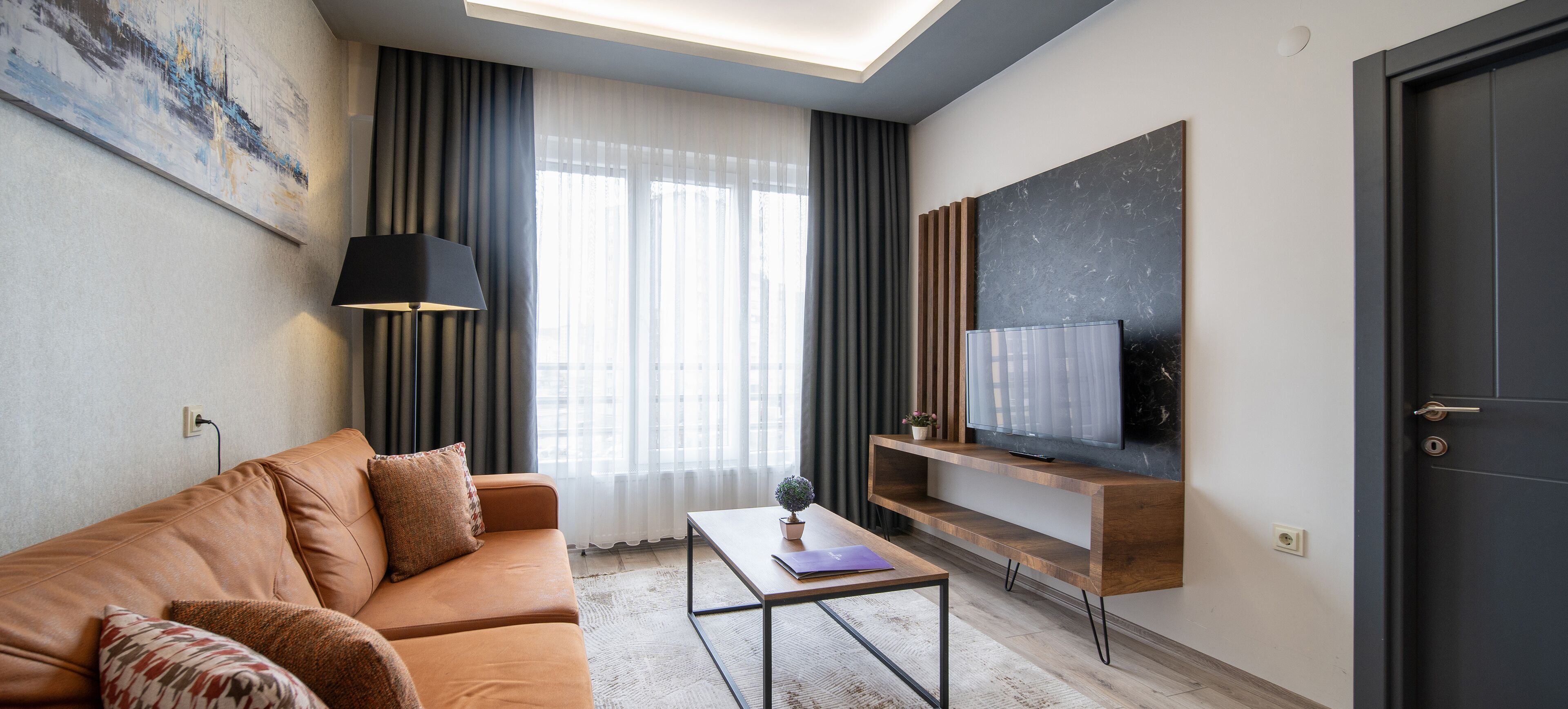 A modern living room with a sofa, a coffee table, a TV mounted on a wooden shelf, and a door.