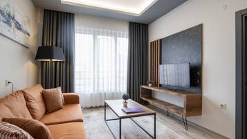 A modern living room with a sofa, a coffee table, a TV mounted on a wooden shelf, and a door.