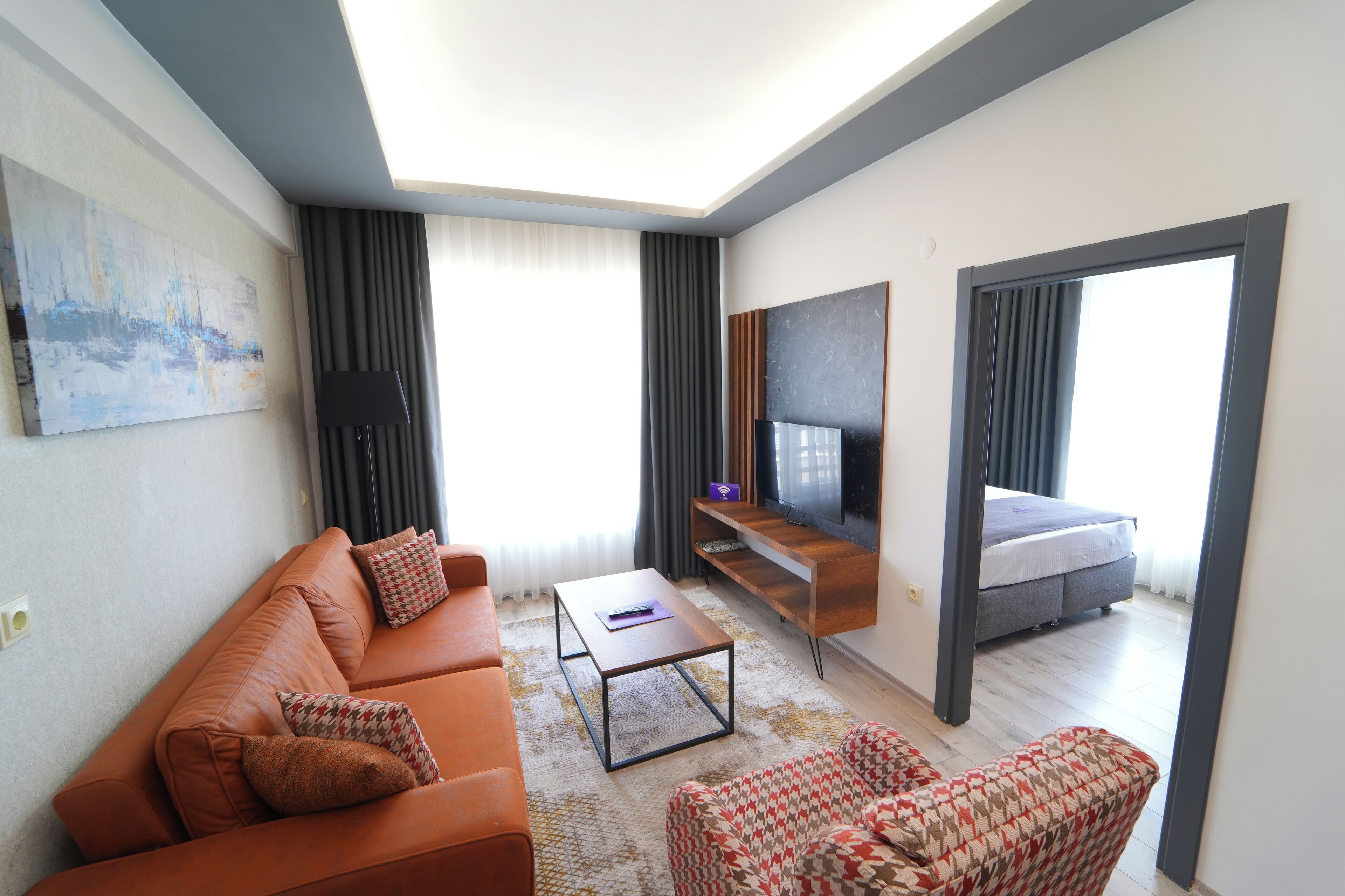 Una habitación de hotel moderna con sofá, sillón, mesa de centro, televisor y cama.