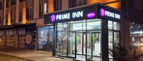 Un hotel con un llamativo letrero que dice "Prime Inn", grandes puertas de cristal y fachada de ladrillo.